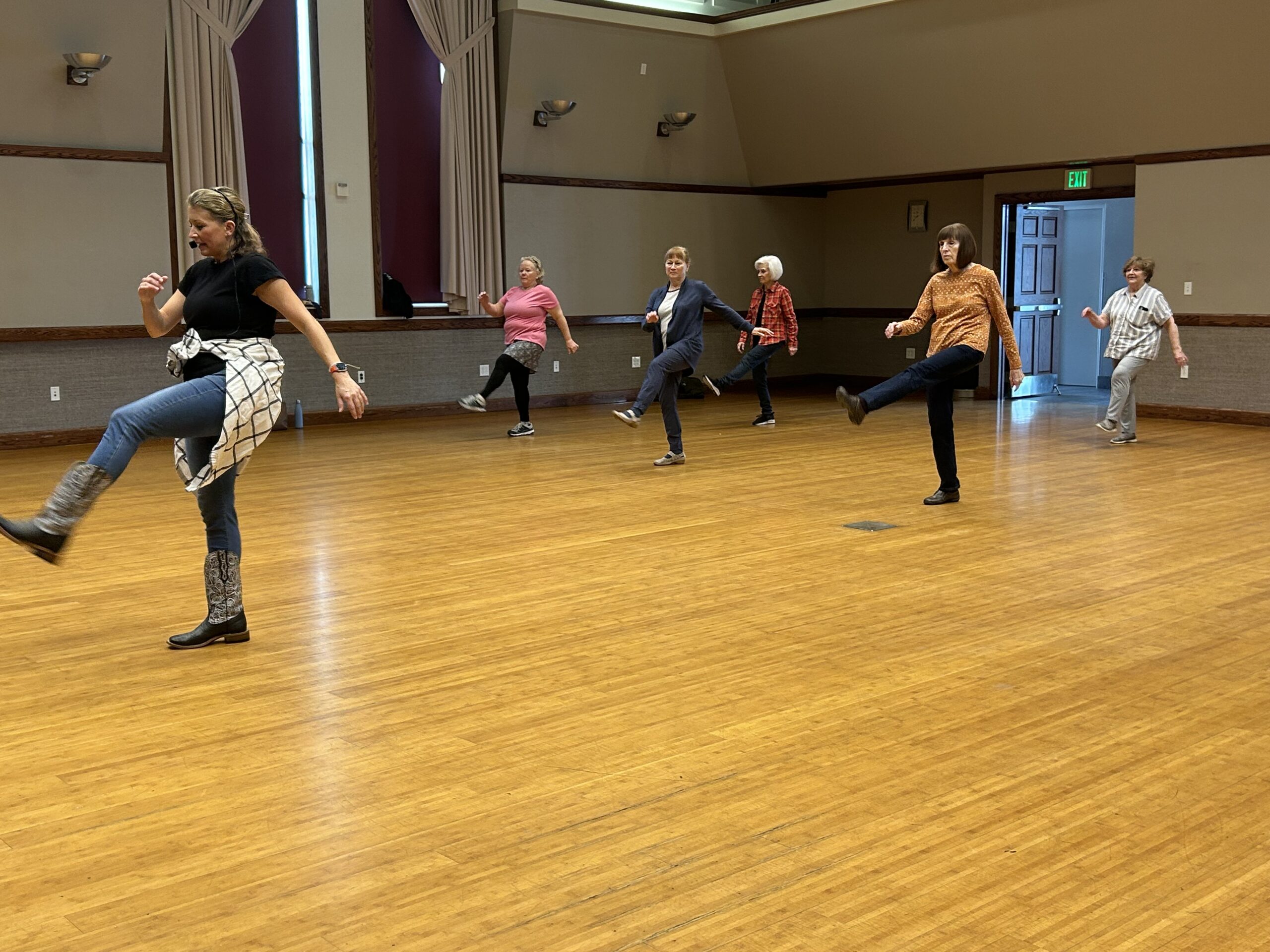 Five active aging participants shown taking direction from line dancing instructor.