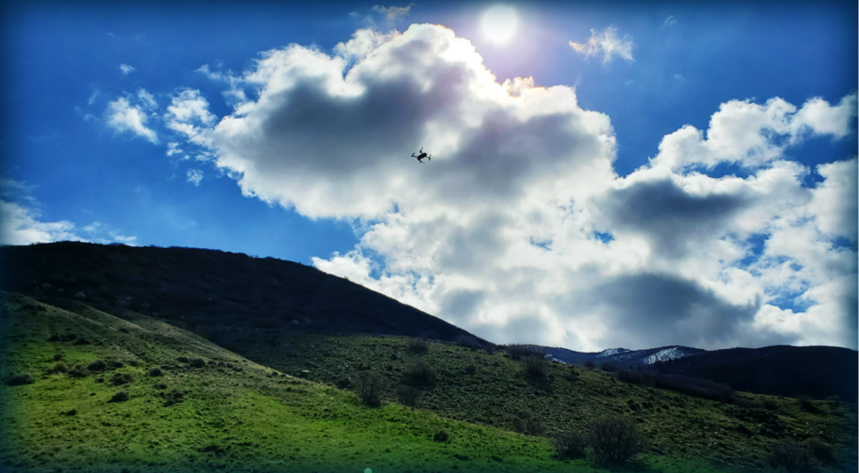 Drone flying in a cloudy sky above green hills